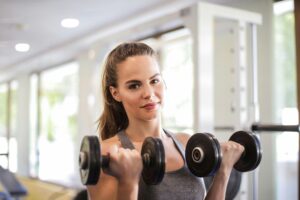 Woman exercising with dumbbells in a bright, modern gym, showcasing fitness and strength.